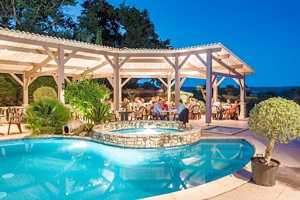 A pool area with a covered seating area and a hot tub.