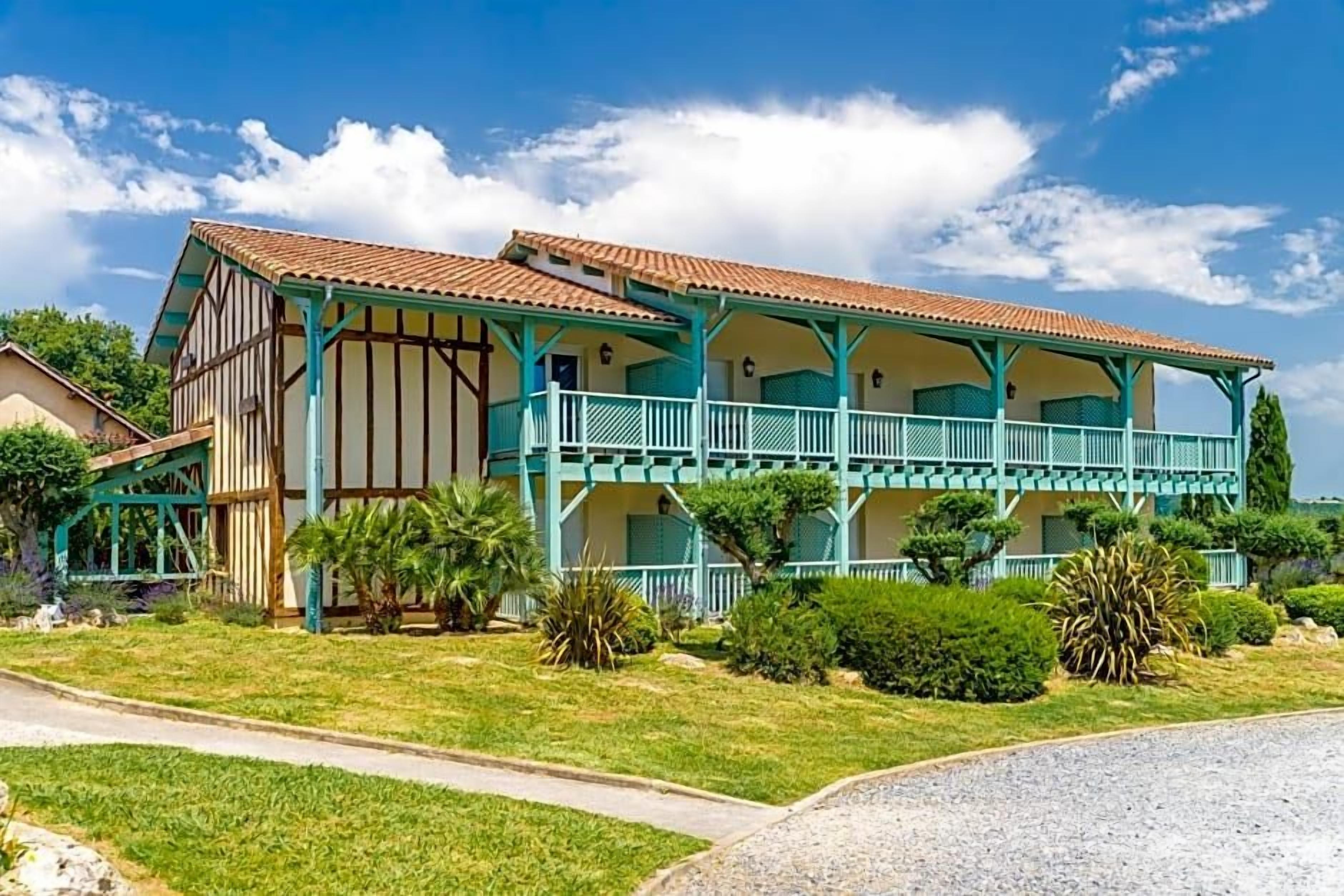 A two-story building with a balcony, surrounded by greenery and a clear sky.