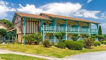 A two-story building with a balcony, surrounded by greenery and a clear sky.
