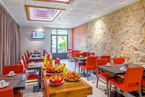 A hotel dining area with tables and chairs, a stone wall, and a television on the wall.
