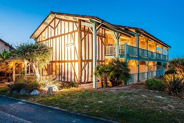 A two-story building with a balcony on the upper floor, surrounded by greenery.