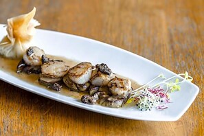 A plate of seared scallops with mushrooms and a garnish of microgreens on a white plate.