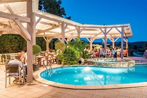 An outdoor pool area with a covered seating area and a stone fountain.