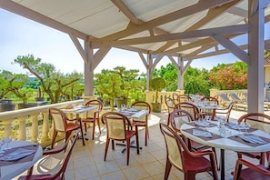 Une terrasse extérieure avec des tables et des chaises, entourée de verdure et d’arbres.
