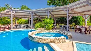 A swimming pool with a stone edge, surrounded by a covered patio area with chairs and tables.