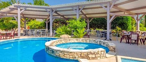 Une piscine bordée de pierres, entourée d’un patio couvert aménagé avec des chaises et des tables.