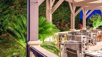 An outdoor patio with tables and chairs, surrounded by lush greenery and flowering plants.