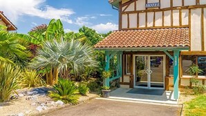 A hotel with a traditional facade, a covered entrance, and lush tropical vegetation.