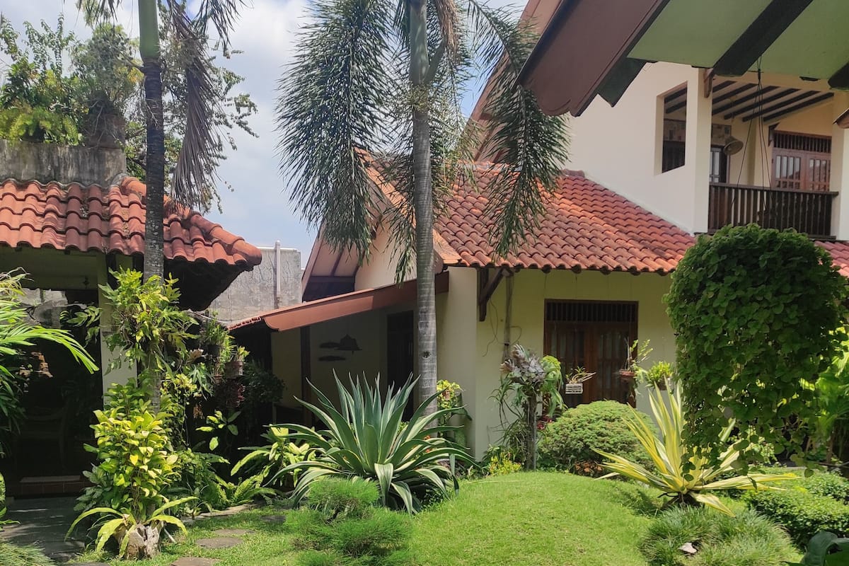 A well-maintained garden with a stone pathway, various plants, and a house with a red-tiled roof.