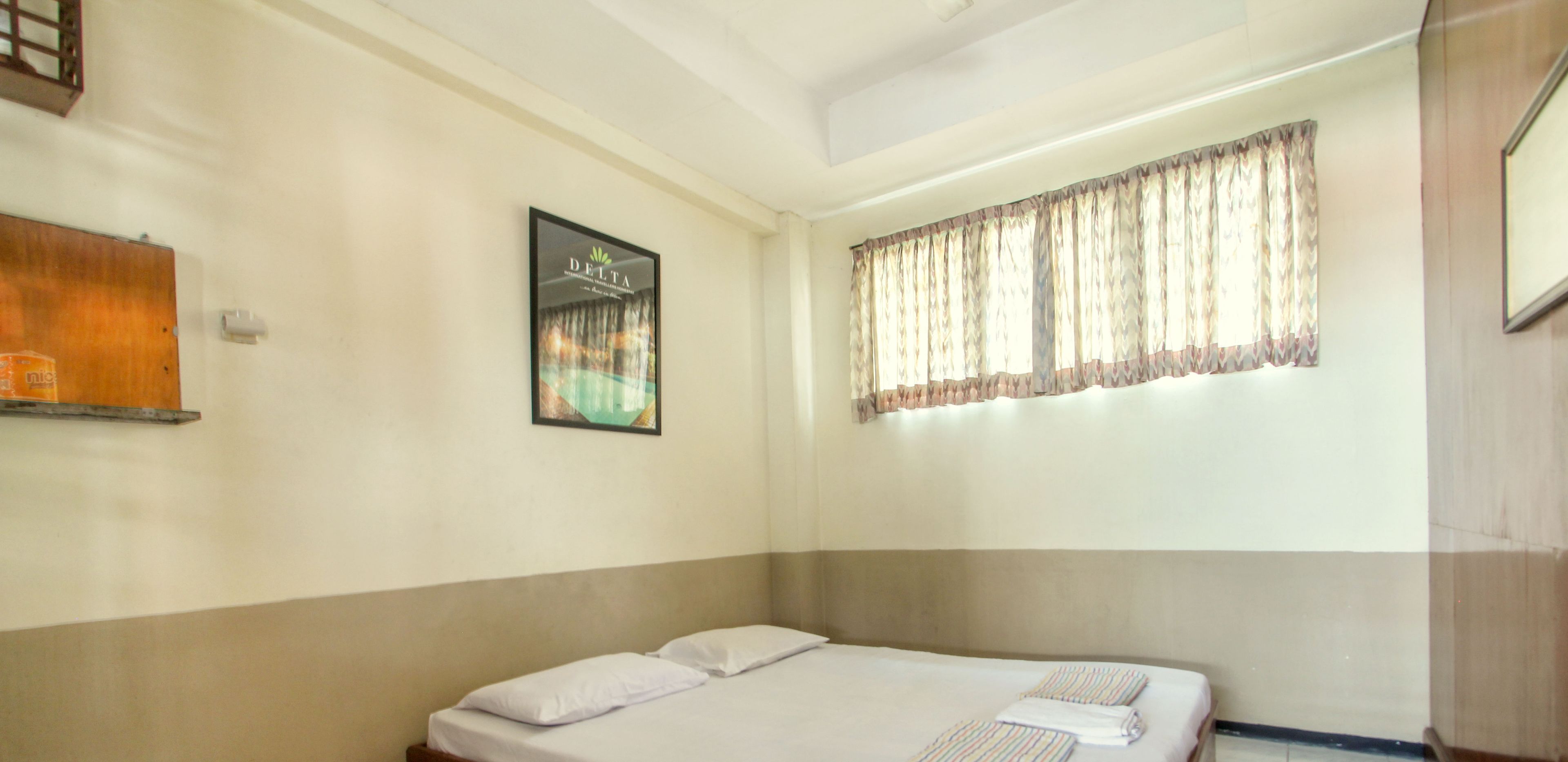 A single bed with white bedding, a window with patterned curtains, and a wall-mounted picture frame.