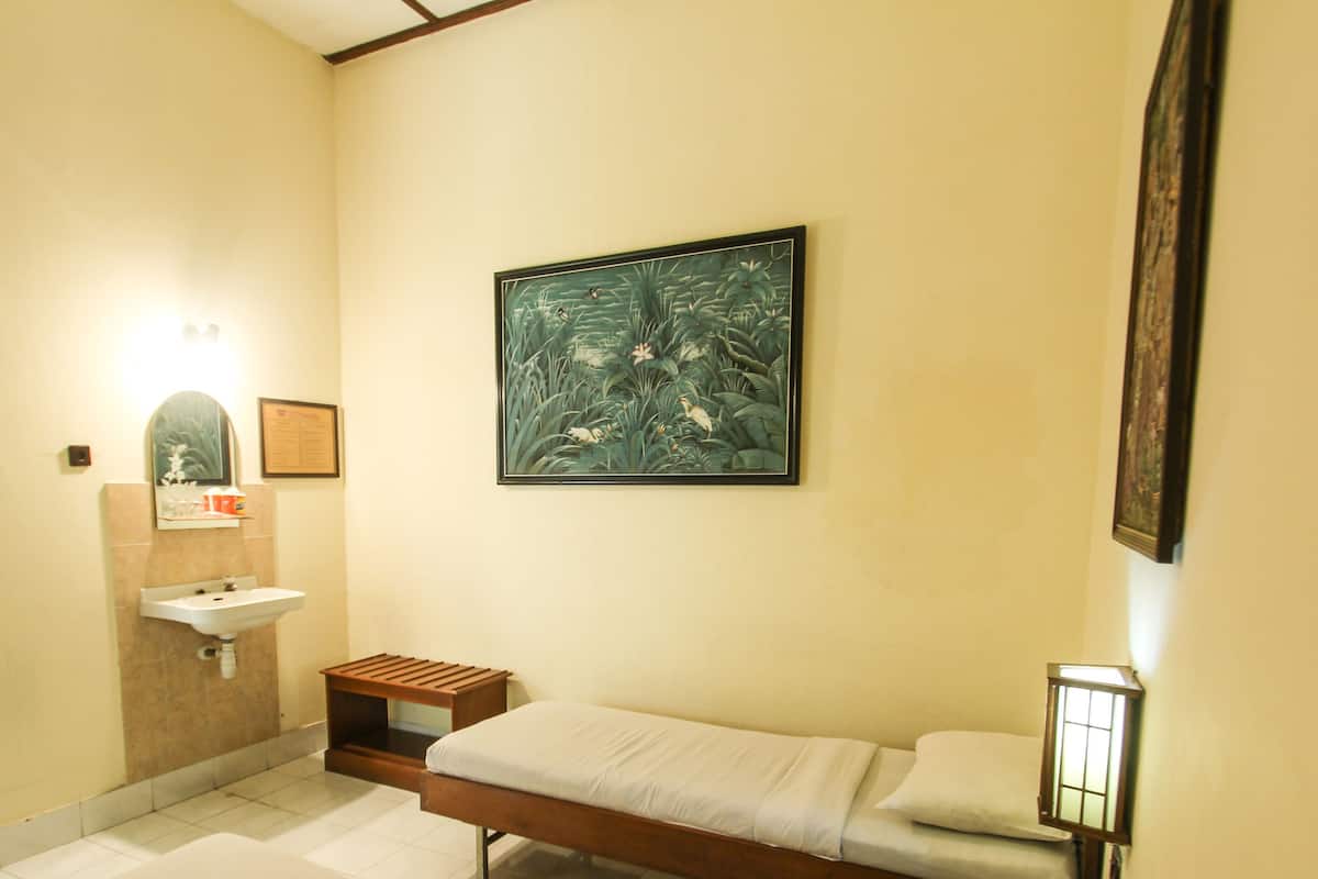 A small, clean room with a single bed, a sink, and a framed painting on the wall.