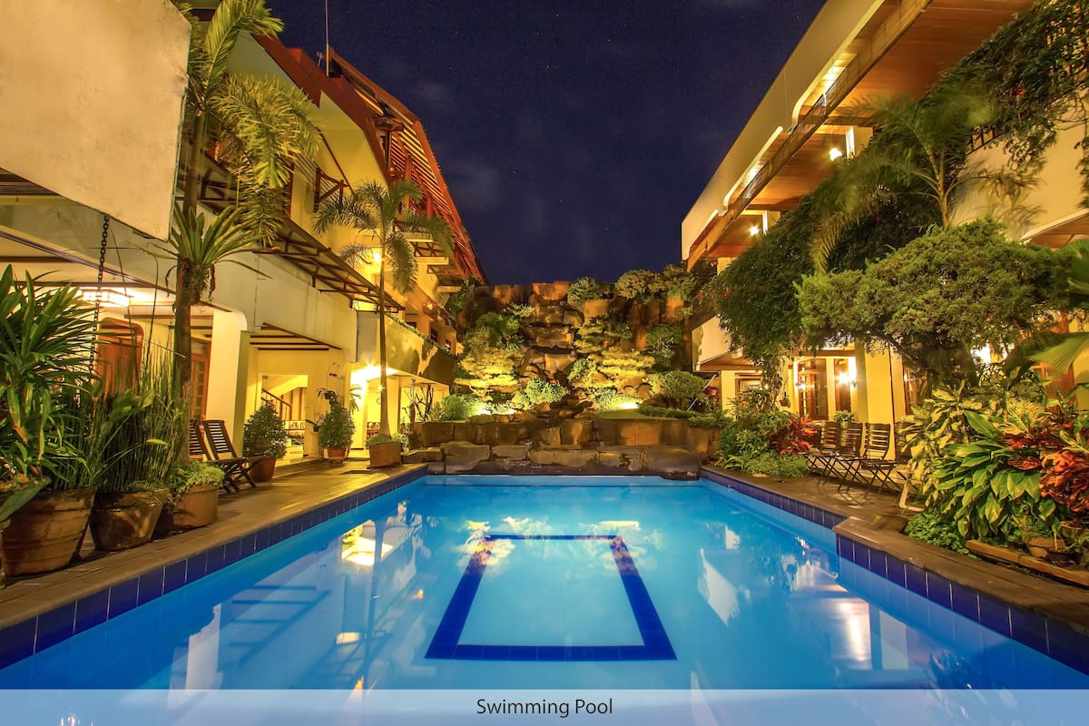 A swimming pool with a clear blue water feature, surrounded by lush greenery and architectural elements.