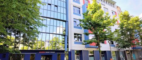 Un edificio moderno con fachada azul y blanca, una entrada visible y un árbol en la parte delantera.