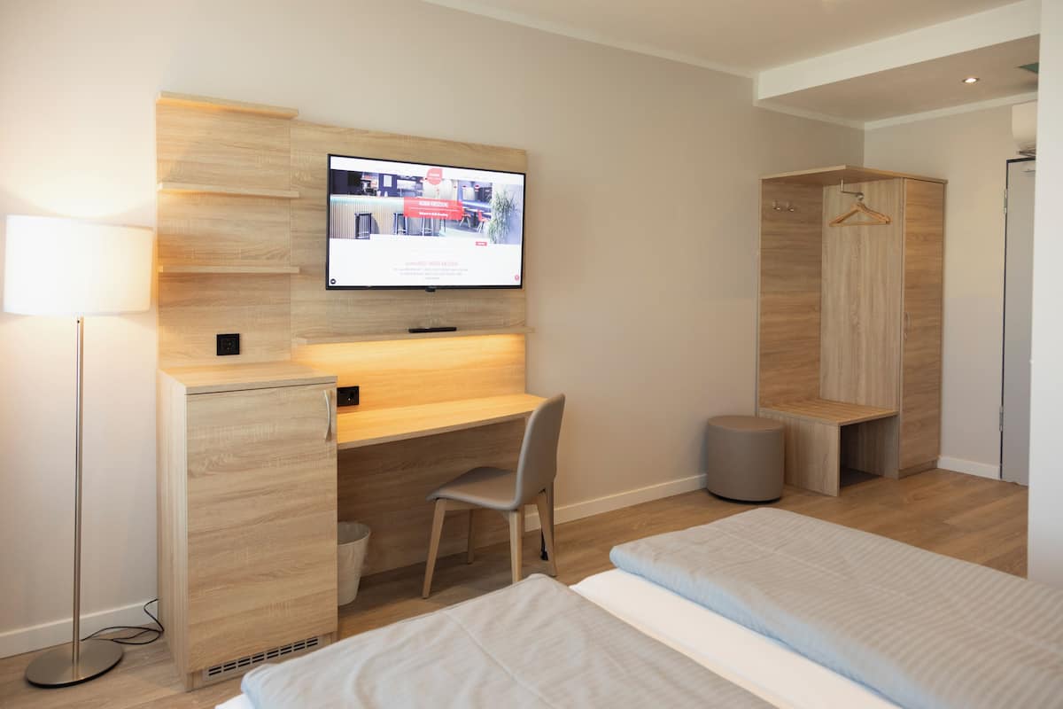 Quarto de hotel moderno com uma mesa de madeira, televisão montada acima, guarda-roupa e uma cama.