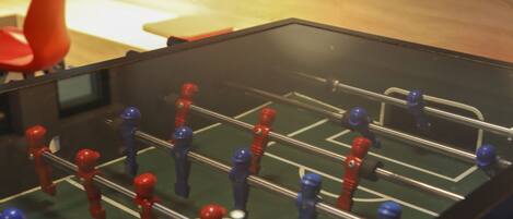 A foosball table in a room with a bed and pillows in the background.