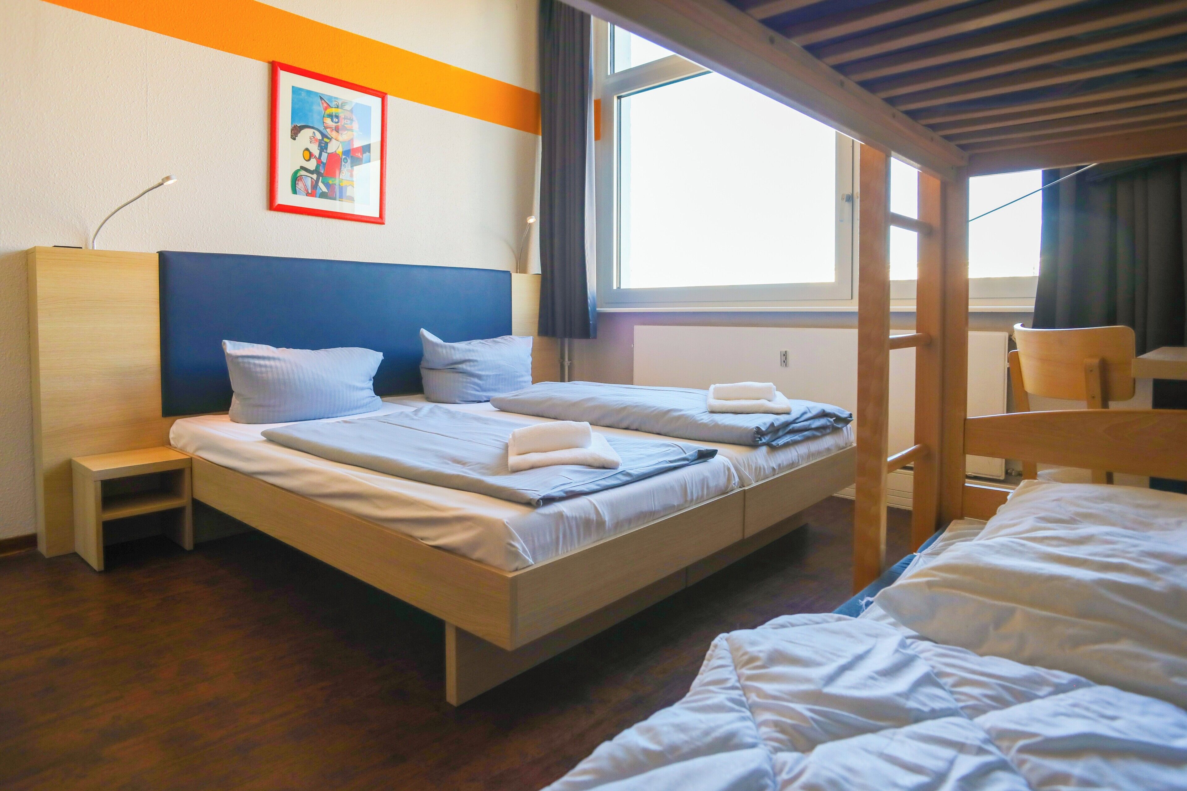 Habitación de hotel con cama, escritorio, silla, ventana y un cuadro en la pared.