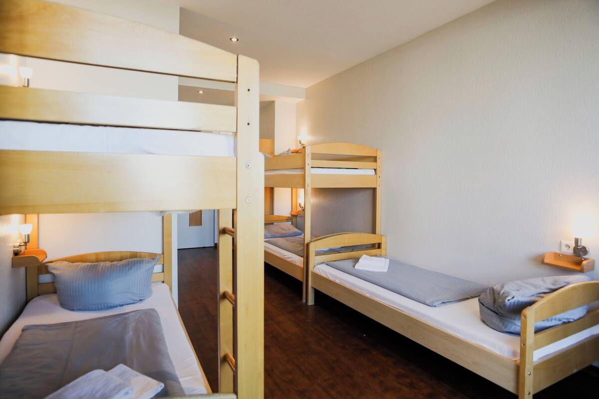 Quarto com beliches, uma mesa de cabeceira com abajur e uma porta que dá para outro cômodo.