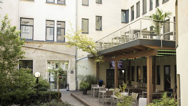Un patio con mobiliario exterior, plantas en macetas y un edificio con varias ventanas y balcones.