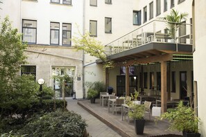 Een binnenplaats met terras, plantenbakken en een gebouw met meerdere ramen en balkons.