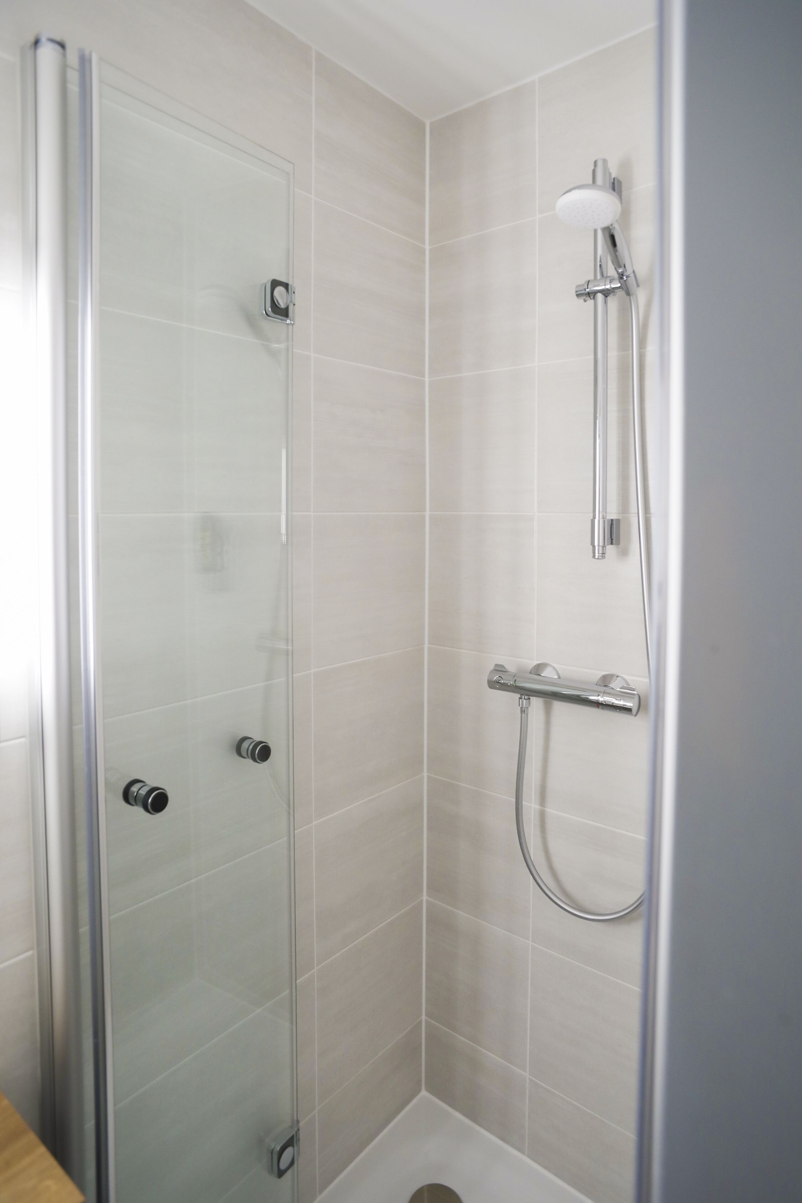 Une cabine de douche fermée par des parois en verre, dotée d’un pommeau de douche à main et d’un robinet fixé au mur.