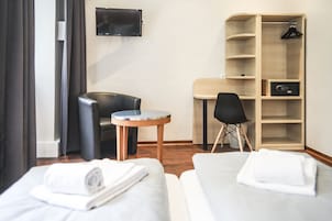 Habitación de hotel con dos camas, un escritorio, una silla, un televisor y un armario.