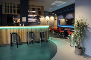 Un área de bar moderna con mostrador de madera, taburetes y sillas rojas.