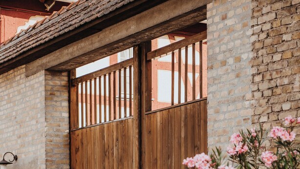 A wooden gate with a brick wall, a cobblestone path, and pink flowers in the foreground. - Kleine Residenz am Schloss (Hochheim am Main)