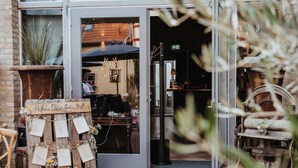 A brick-paved entrance to a building with a glass door, a wooden signboard, and outdoor seating with a table and chairs. - Kleine Residenz am Schloss (Hochheim am Main)