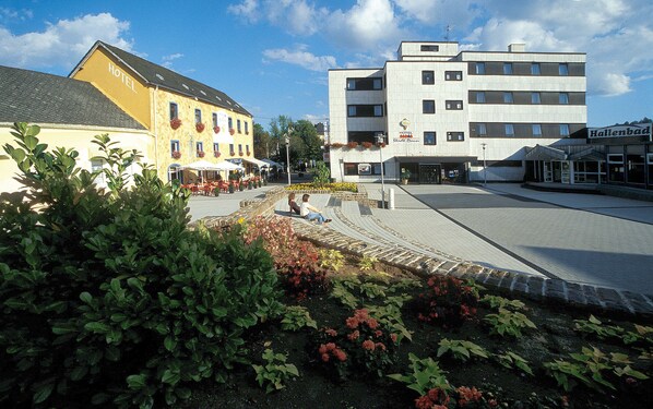 A hotel with a yellow facade and a white building across the street.