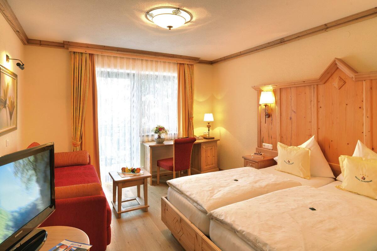 Une chambre d’hôtel avec deux lits, un bureau, une télévision et une fenêtre avec des rideaux.