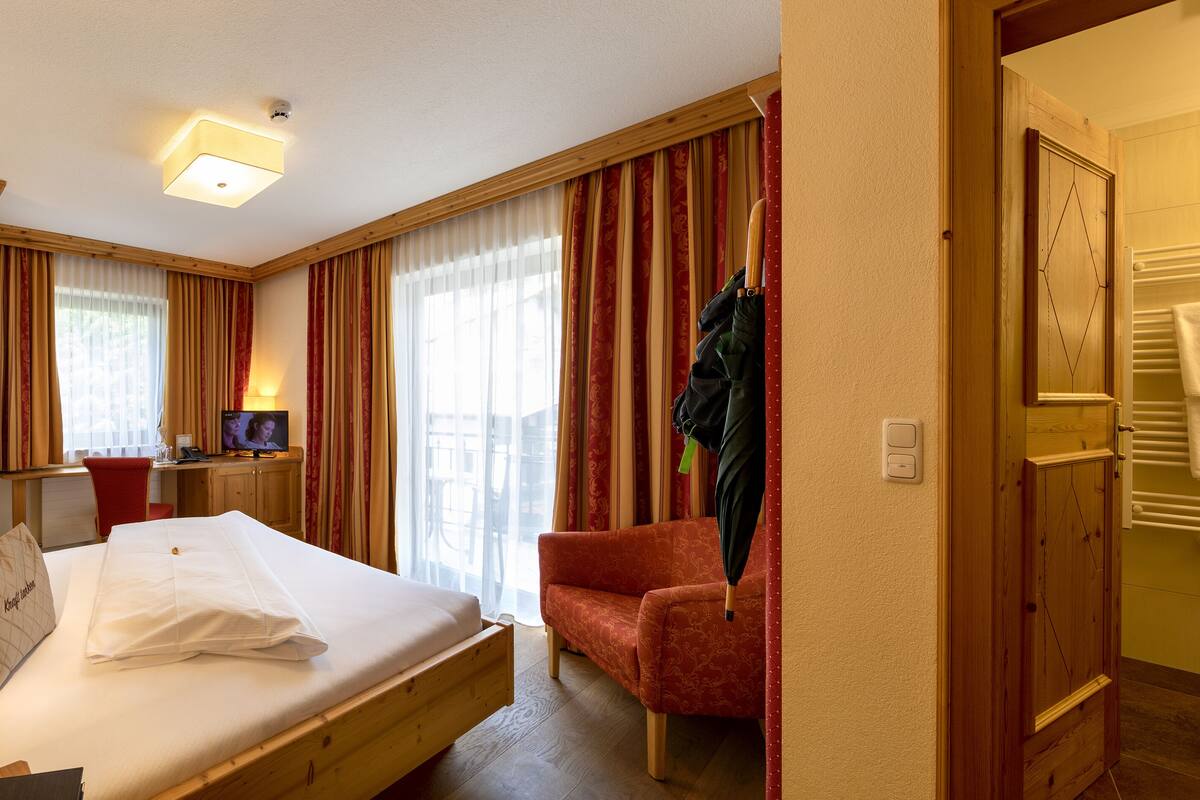 Une chambre d’hôtel avec un lit, un bureau équipé d’un ordinateur, une chaise, une télévision et une fenêtre avec des rideaux.