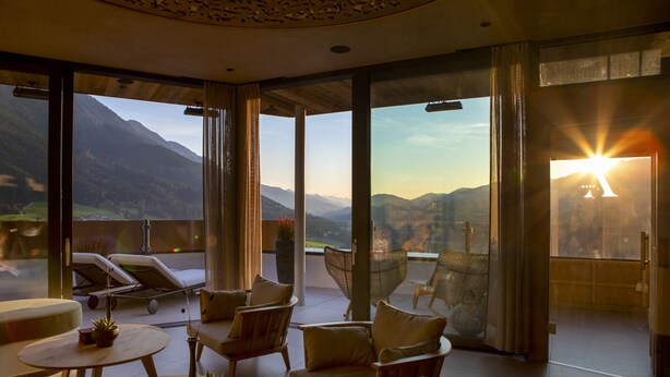 Un vaste balcon offrant une vue sur les montagnes et sur le coucher de soleil. On y trouve plusieurs fauteuils et une petite table agrémentée de plantes.
