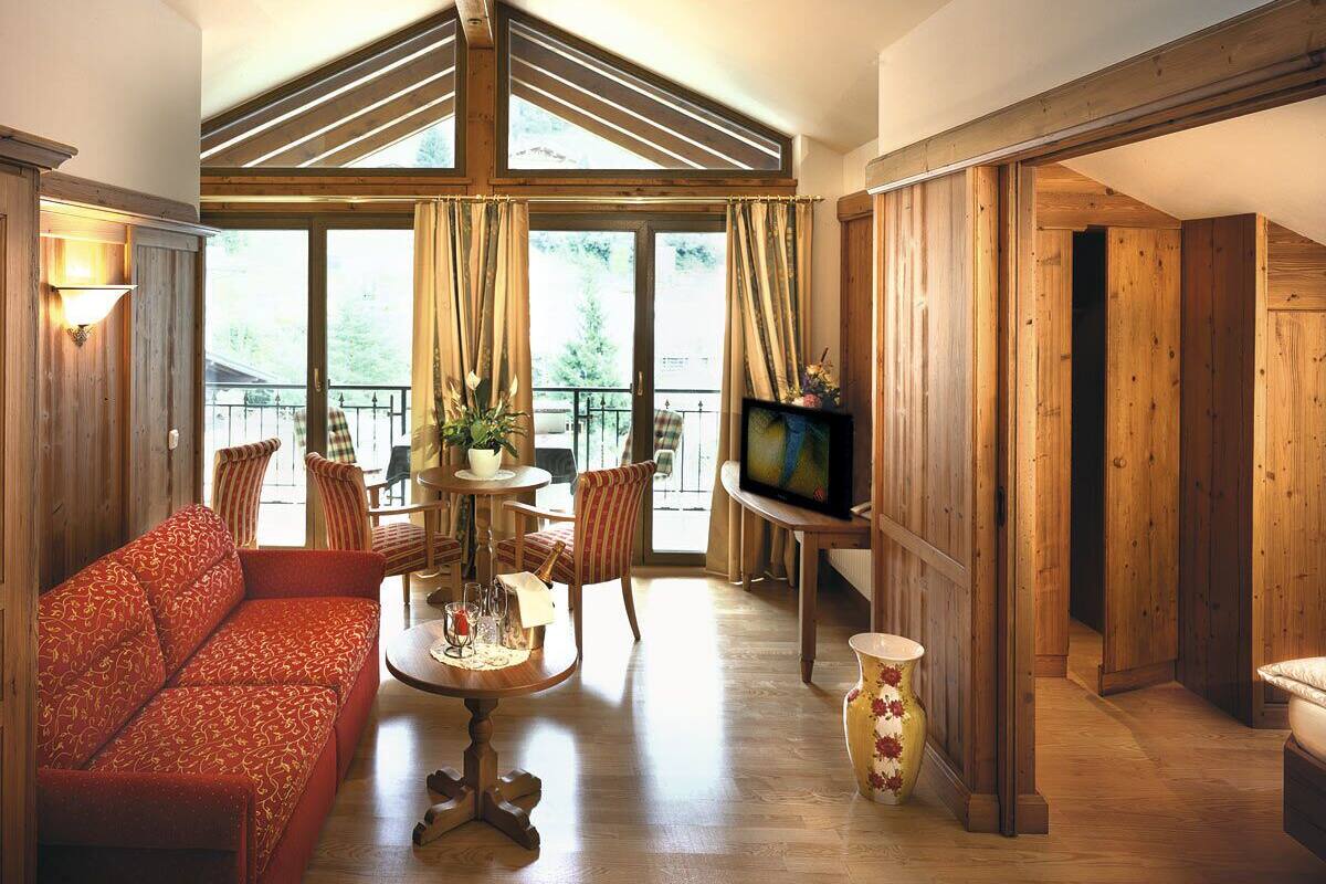 Un salon spacieux avec un canapé rouge, un plancher en bois, un coin repas avec des chaises, un téléviseur et un balcon avec des rideaux.