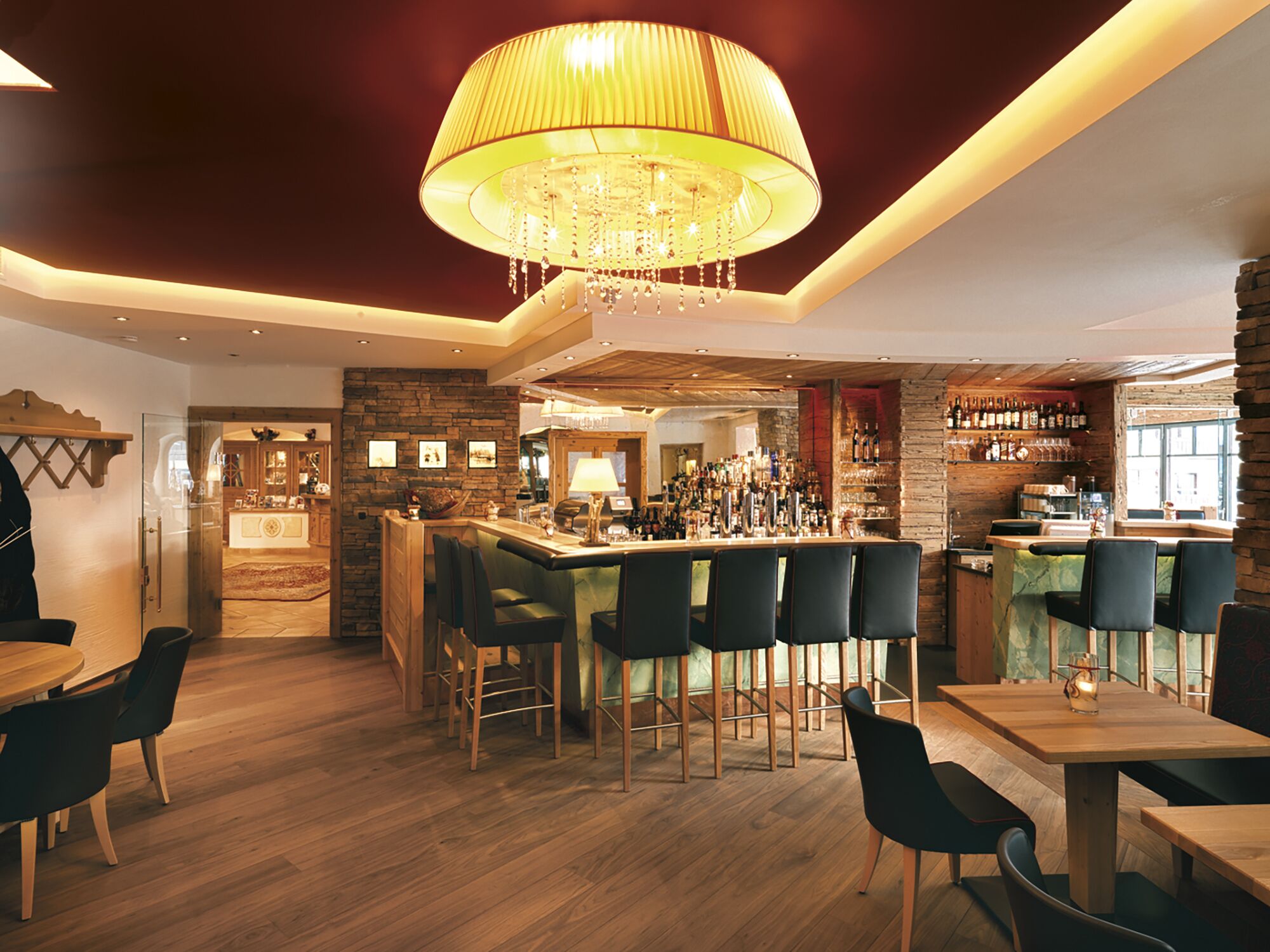 A bar area with wooden flooring, a chandelier, and a bar counter with stools.