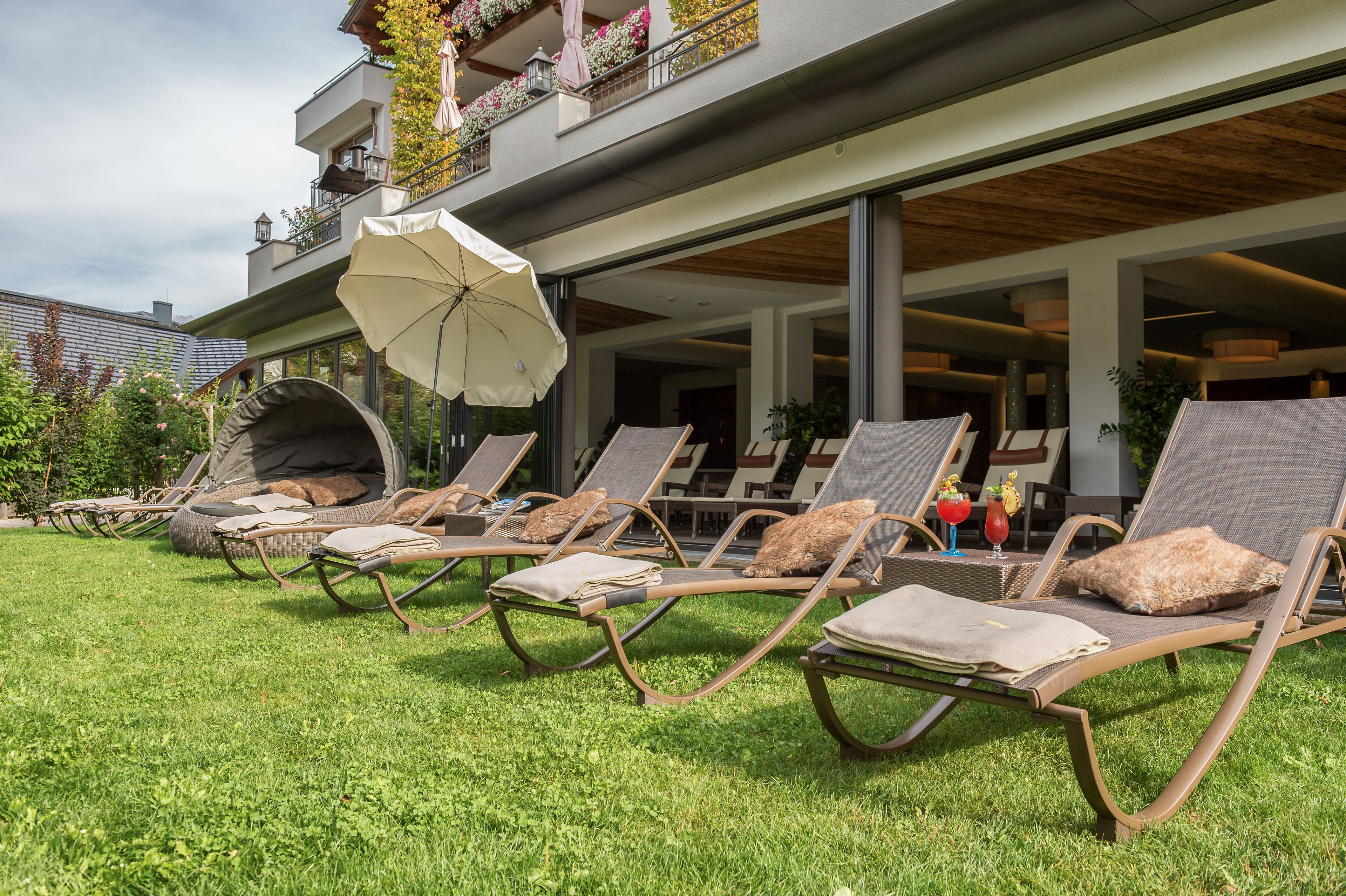 Eine moderne Lounge-Bereich im Freien mit Liegestühlen, einem großen Sonnenschirm und einem gepflegten Rasen.