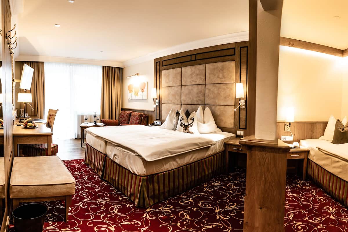 Une chambre d’hôtel avec deux lits, un bureau avec une chaise, un grand miroir et une moquette rouge à motifs.