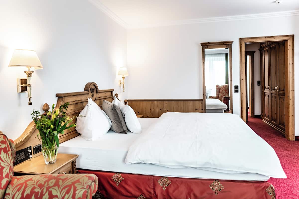 Une chambre d’hôtel avec un lit, des lampes de chevet, un vase de fleurs, un fauteuil rouge recouvert de tissu et des portes de placard en bois.