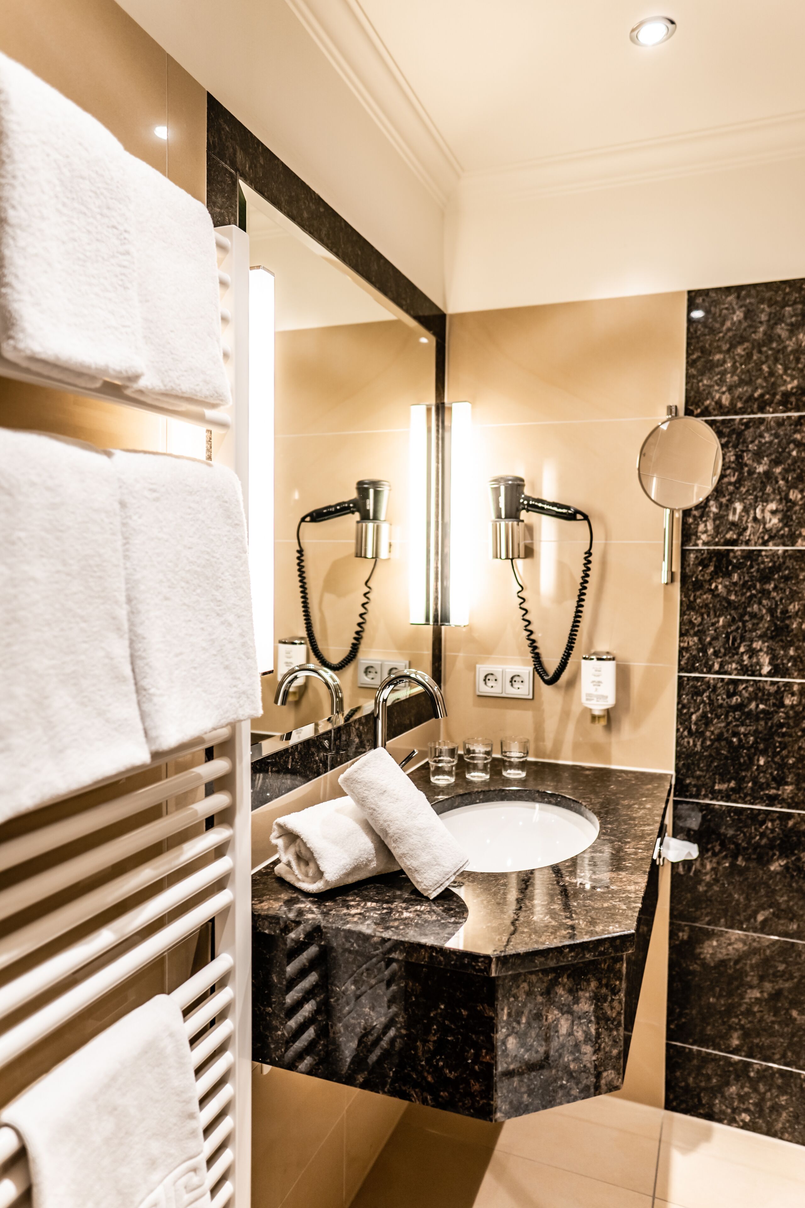 Un baño moderno con lavamanos de mármol, un espejo grande y dos secadores de pelo.