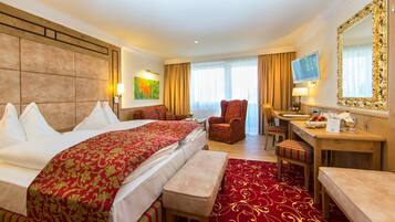 Ein Hotelzimmer mit einem großen Bett, einem Schreibtisch, einem Sessel und einem Fernseher.