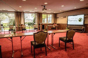 Un salón de conferencias con una gran pantalla mostrando 'Hotel Restaurant Seminar Hubertushof'.