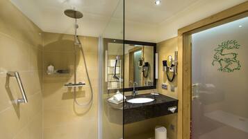 Un baño moderno con ducha envuelta en vidrio, lavamanos con encimera de mármol y puerta de madera con un emblema decorativo.