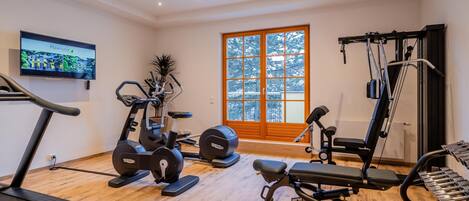 Een sportschool thuis met een loopband, elliptische trainer, gewichtbank en diverse fitnessapparaten.