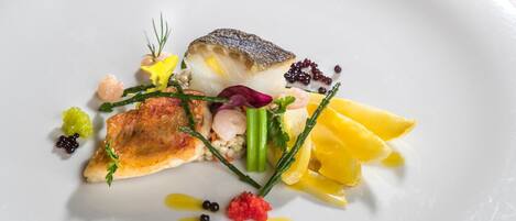A white plate with a variety of food items including fish, vegetables, and garnishes.