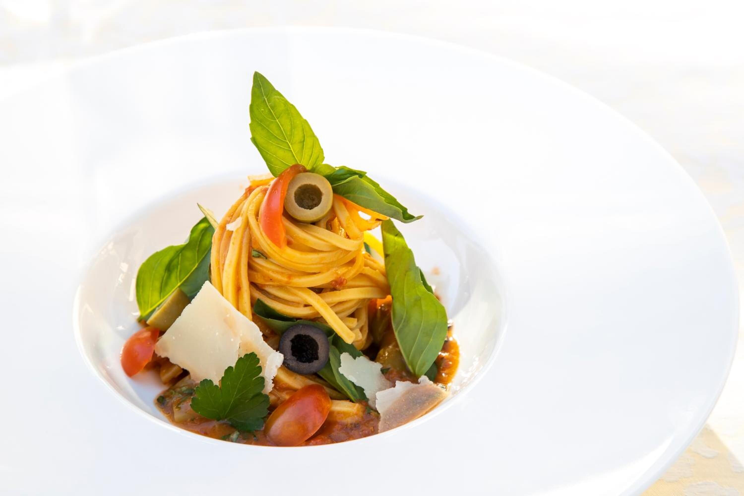 Une assiette de spaghettis agrémentés de basilic, d’olives et de fromage.