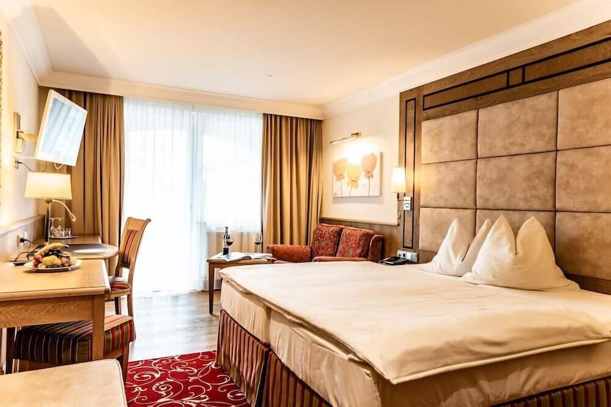 Une chambre d’hôtel avec un grand lit, un bureau avec une chaise, une télévision et une fenêtre avec des rideaux.