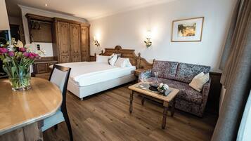A hotel room with a bed, a sofa, a wooden coffee table, a dining table with a vase of flowers, and a kitchen area.