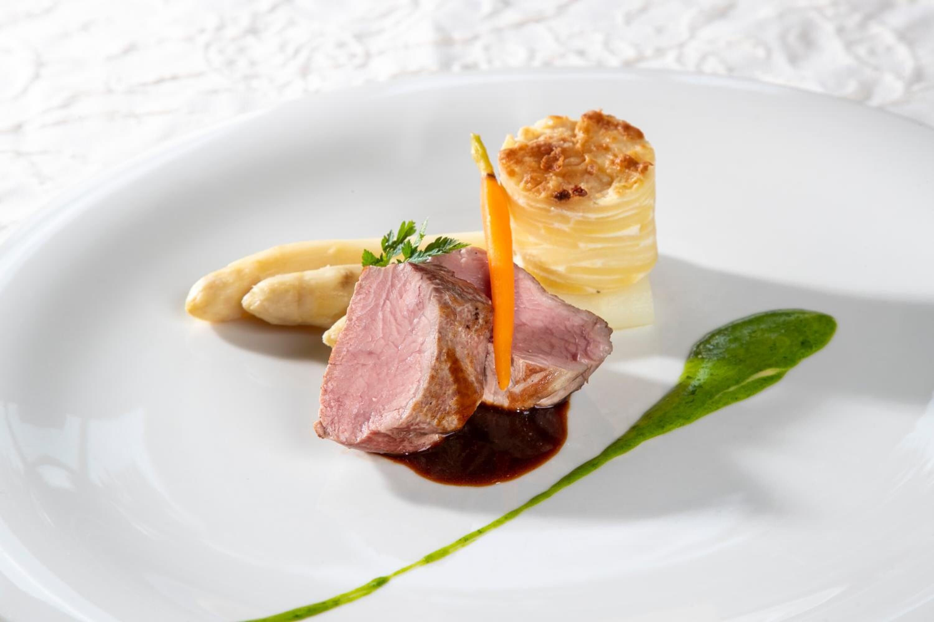A white plate with a piece of meat, a pastry, and a green leaf garnish.