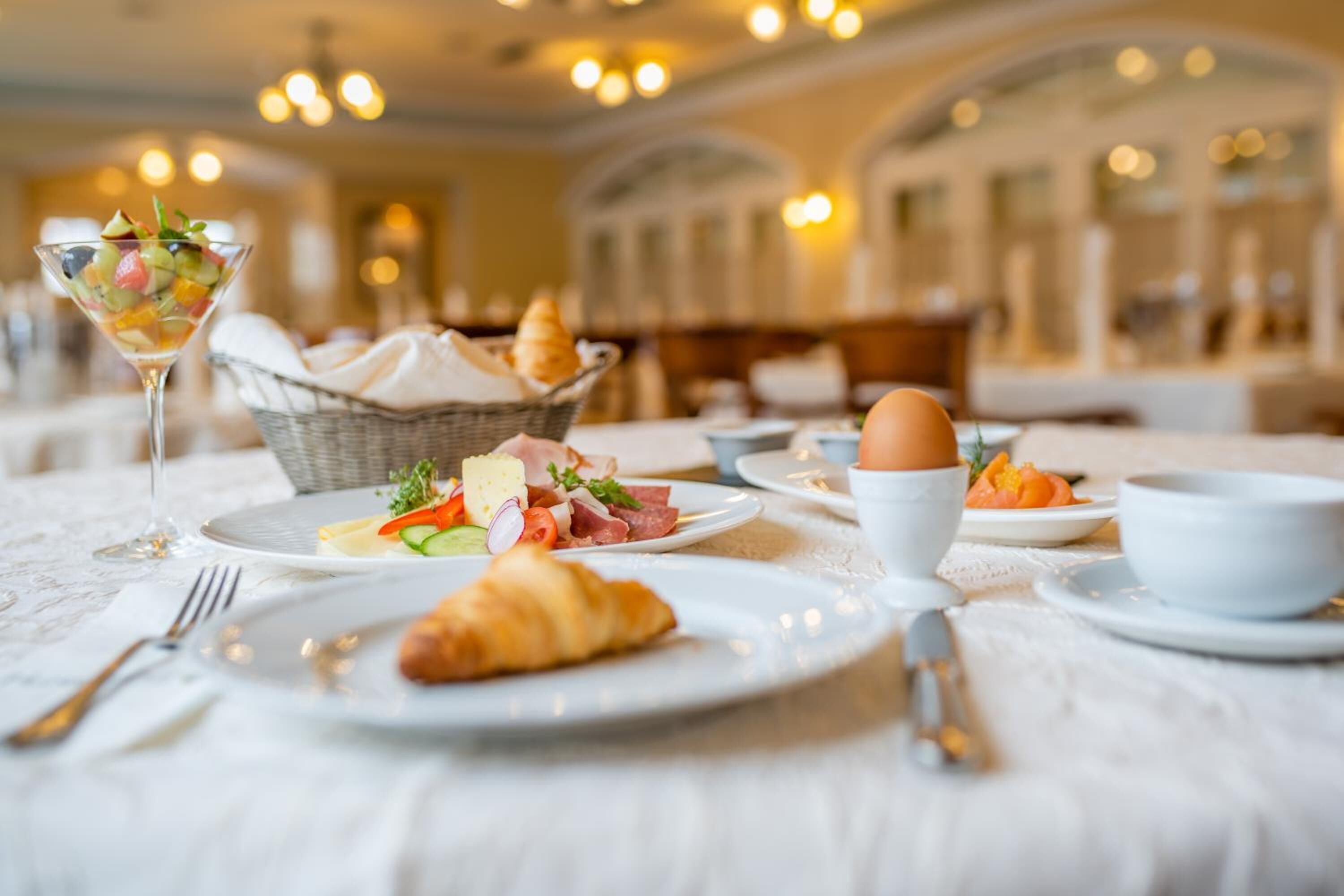 A breakfast setting with croissants, a fruit salad, and a basket of bread on a table.