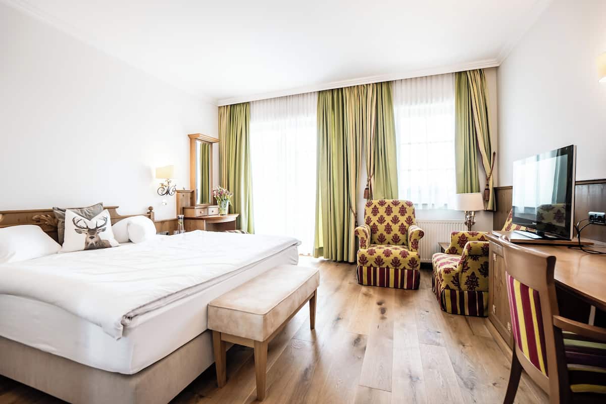 Une chambre d’hôtel avec un grand lit, une chaise, un bureau, une télévision et une fenêtre avec des rideaux.