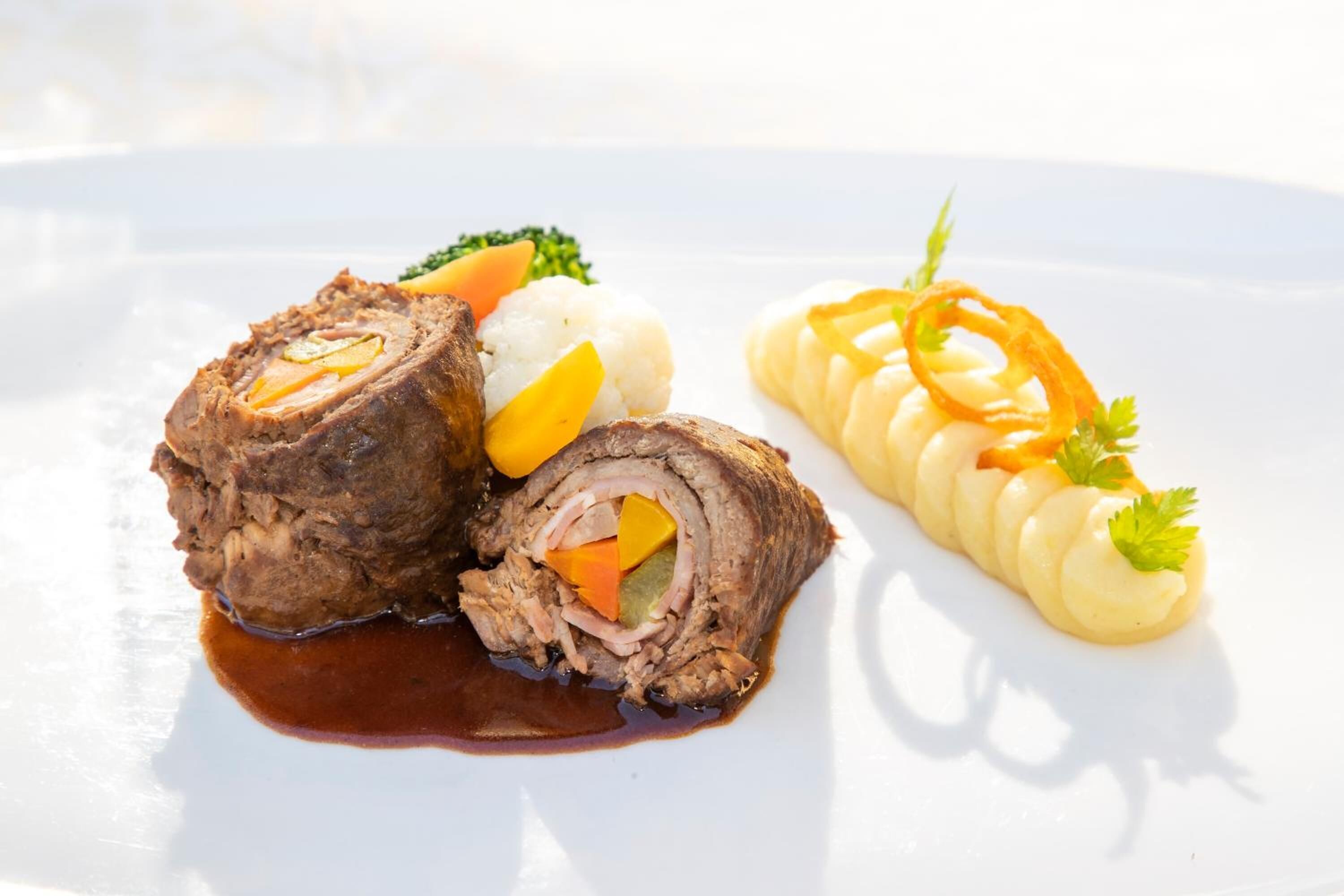 A plate with a rolled meat dish, mashed potatoes, and a side of carrots.